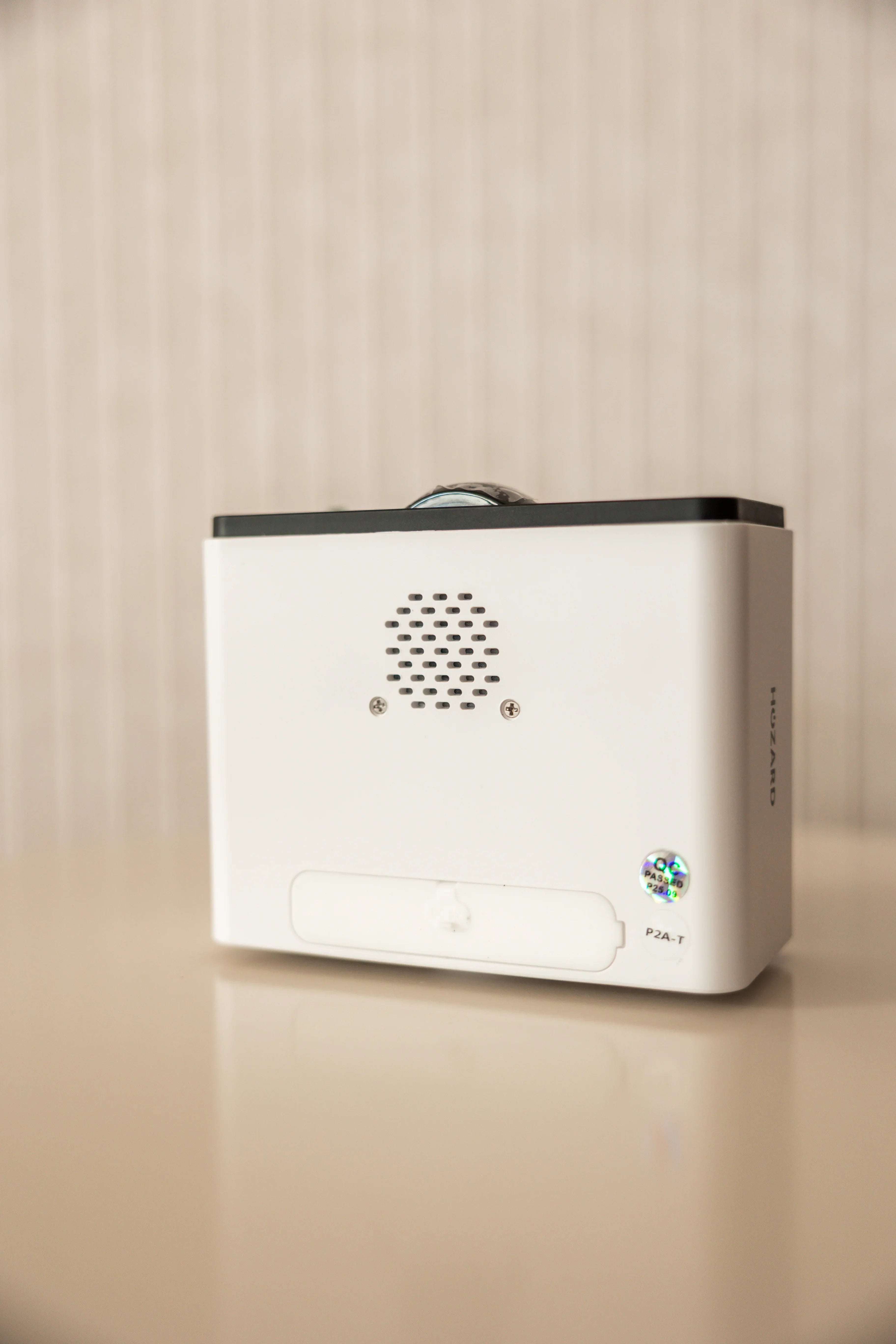 Witte elektronische beveiligingsunit op tafel met ventilatierooster en hologramsticker