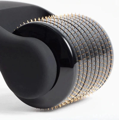 Close-up van een zwarte dermaroller met fijne gouden naaldjes, beauty product.