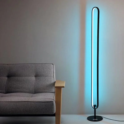 Moderne staande LED lamp met blauw licht naast een grijze bank in een minimalistisch interieur.