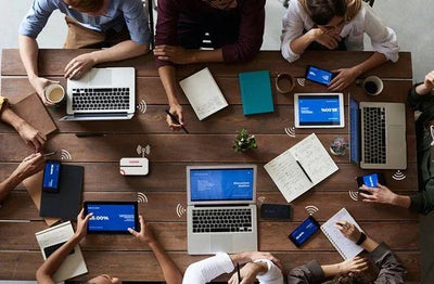 Groep mensen werkt rond tafel met laptops, tablets en draadloze elektronica gadgets.