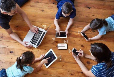 Gezin op houten vloer gebruikt tablets, smartphone en laptop verbonden met draagbare wifi-router.